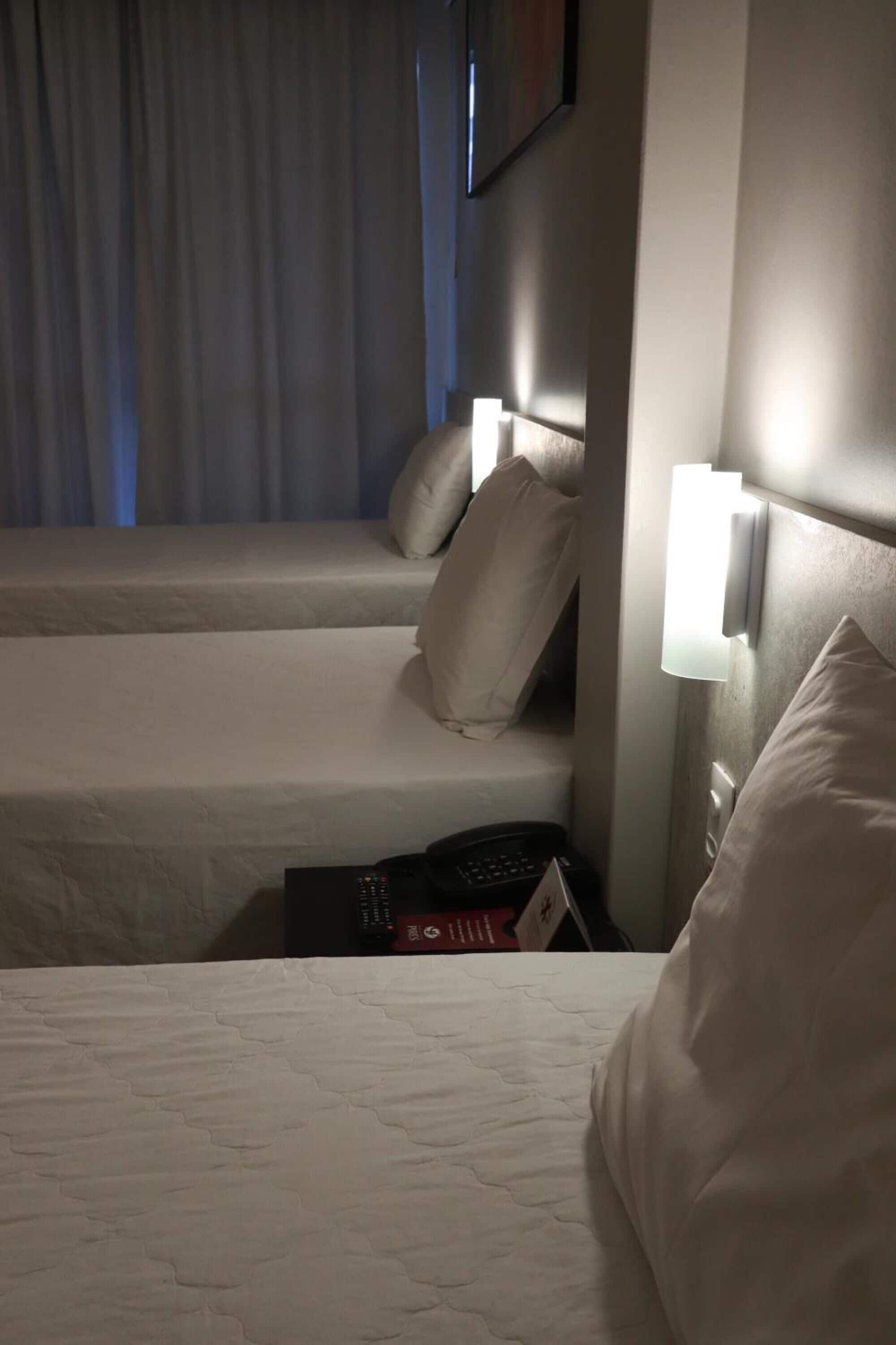 Habitación de hotel con dos camas, cada una con una almohada y una lámpara de noche.
