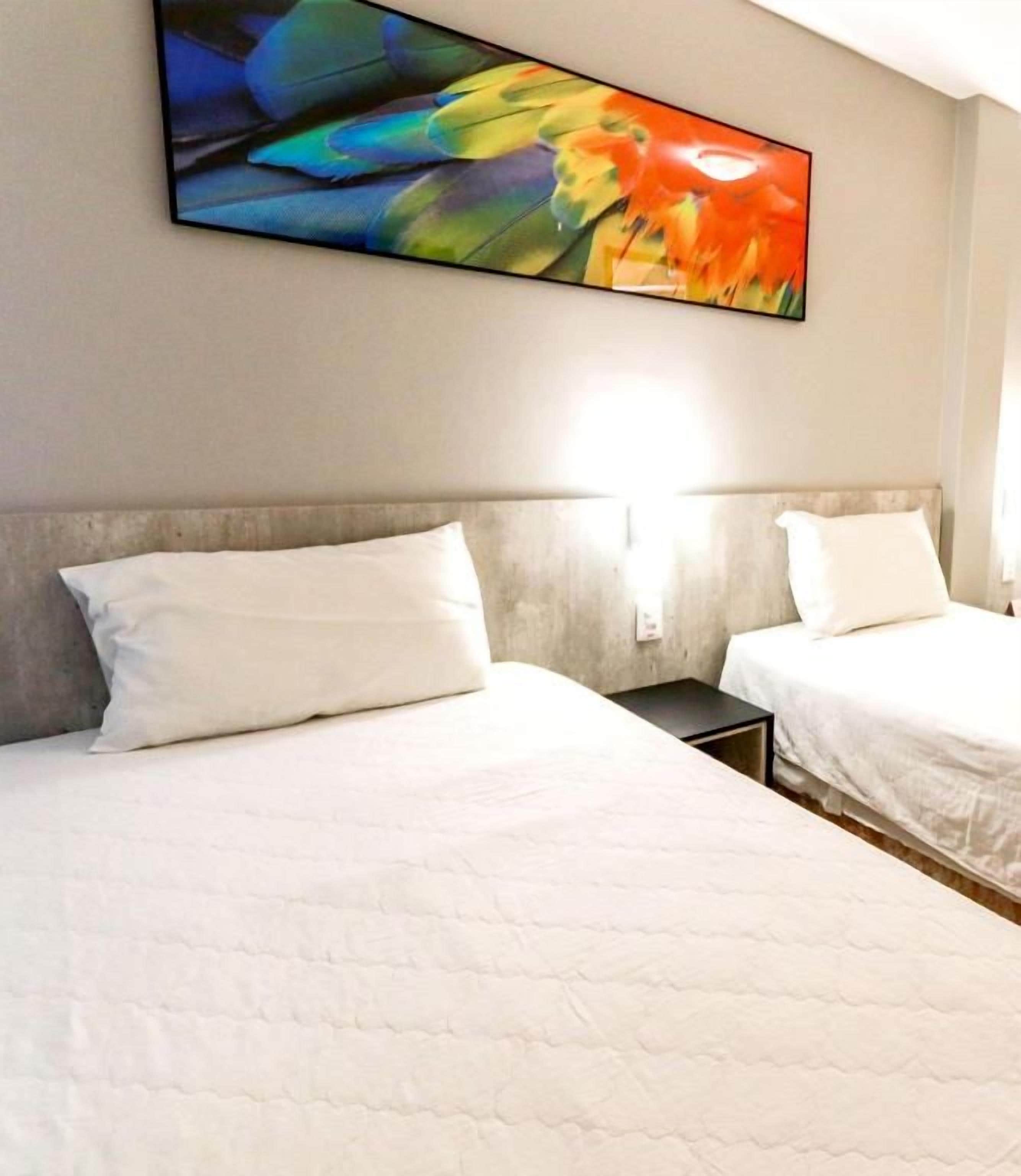 Habitación de hotel con dos camas, un televisor montado en la pared y una mesita de noche.