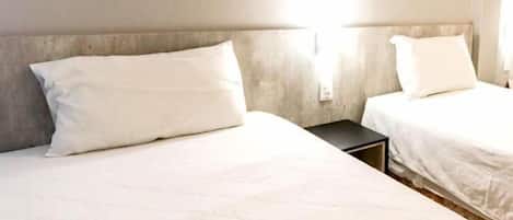 A hotel room with two beds, a wall-mounted TV, and a bedside table.