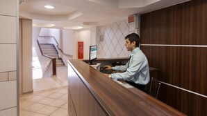 Una reception con una scrivania e un computer, una scala sullo sfondo e un cartello con la scritta "SAIDA".