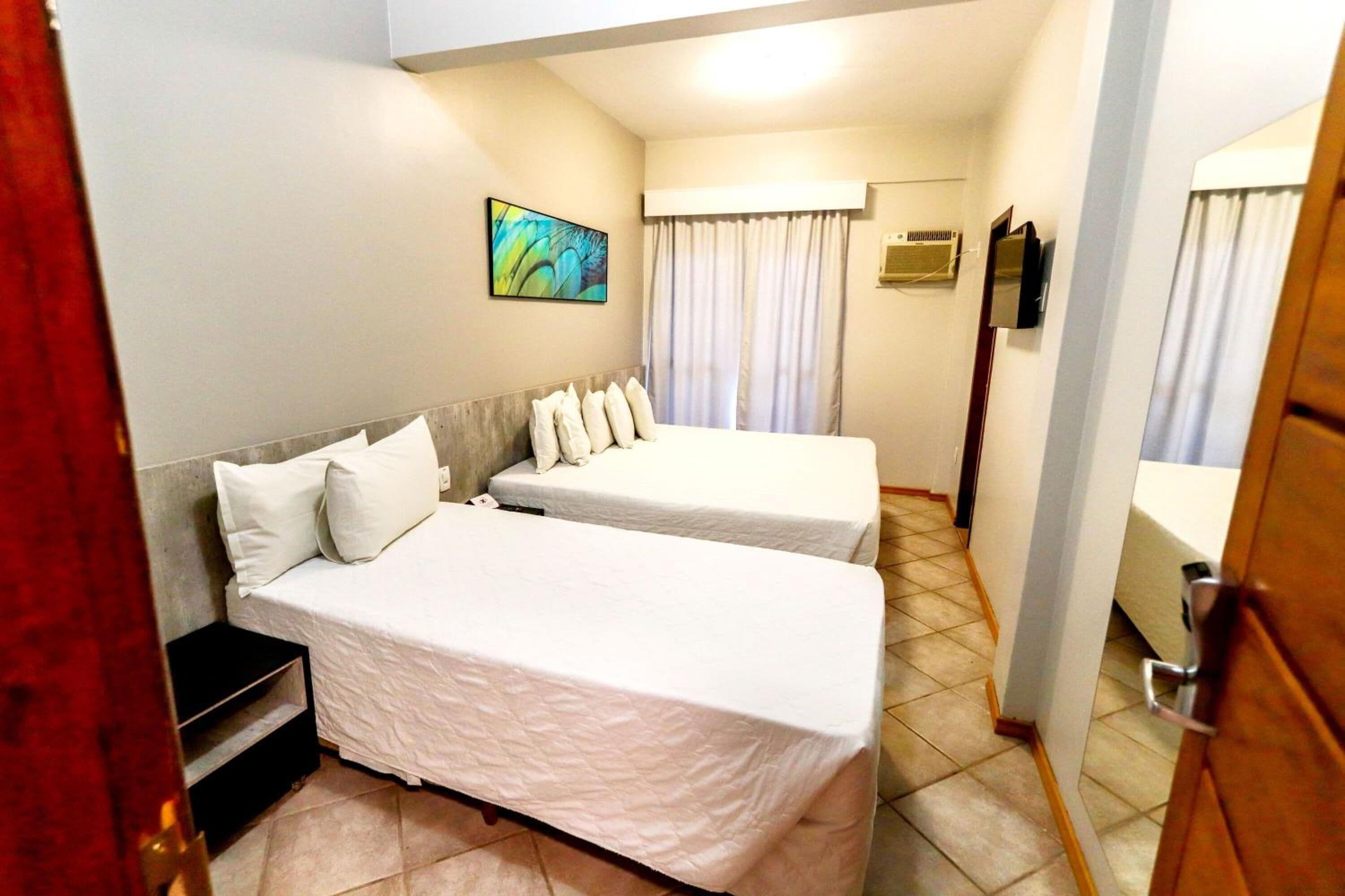 Une chambre d’hôtel avec deux lits, un tableau au mur, un appareil de climatisation et une salle de bain avec un miroir et des rideaux.