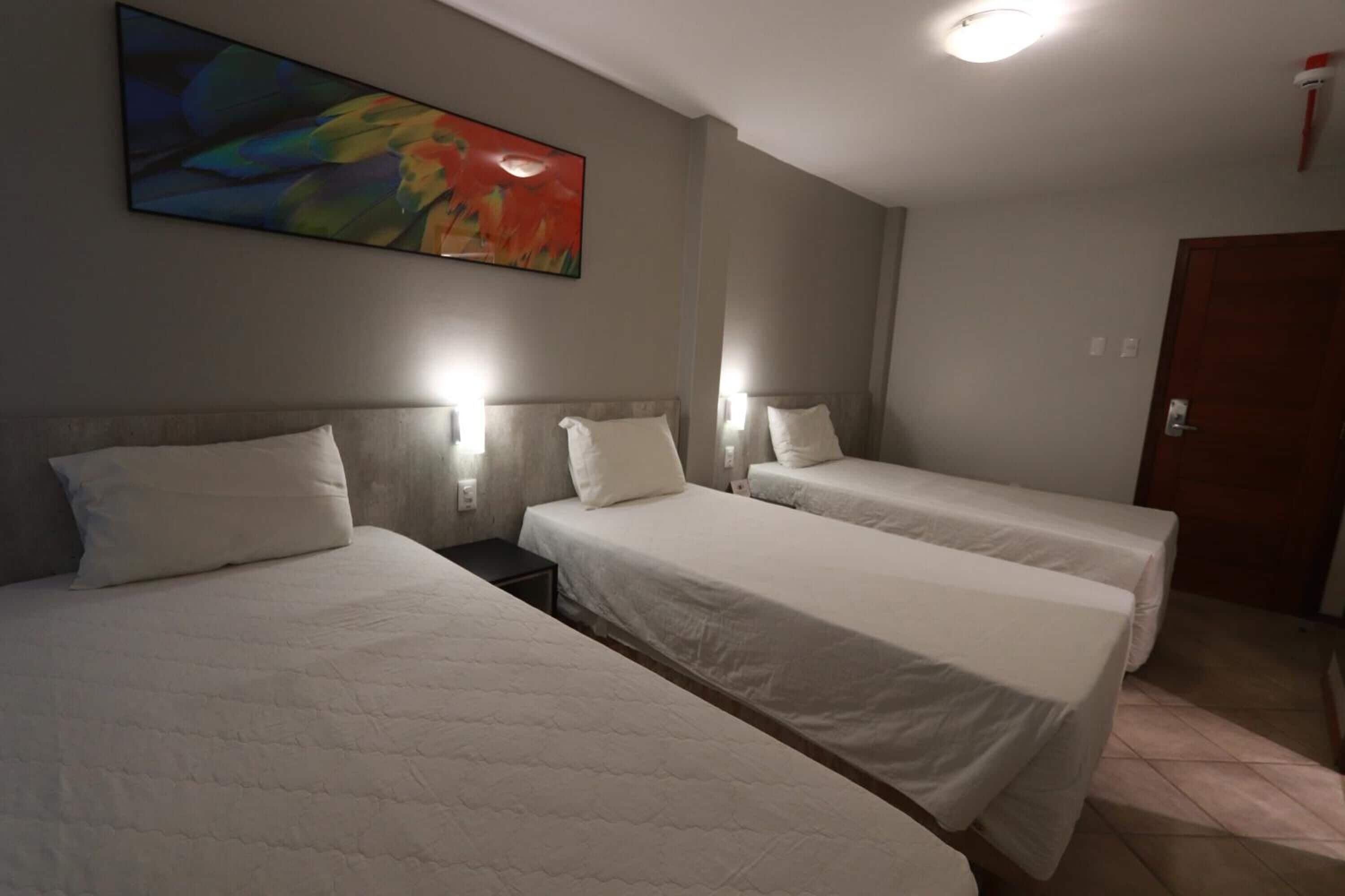 A hotel room with two single beds, a painting on the wall, and a door to the right.