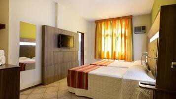 Habitación de hotel con cama, televisión, espejo y ventana con cortinas.