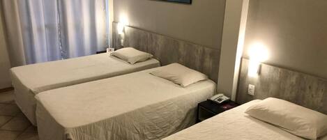 Quarto de hotel com duas camas de solteiro, uma mesa de cabeceira com telefone e um quadro na parede.