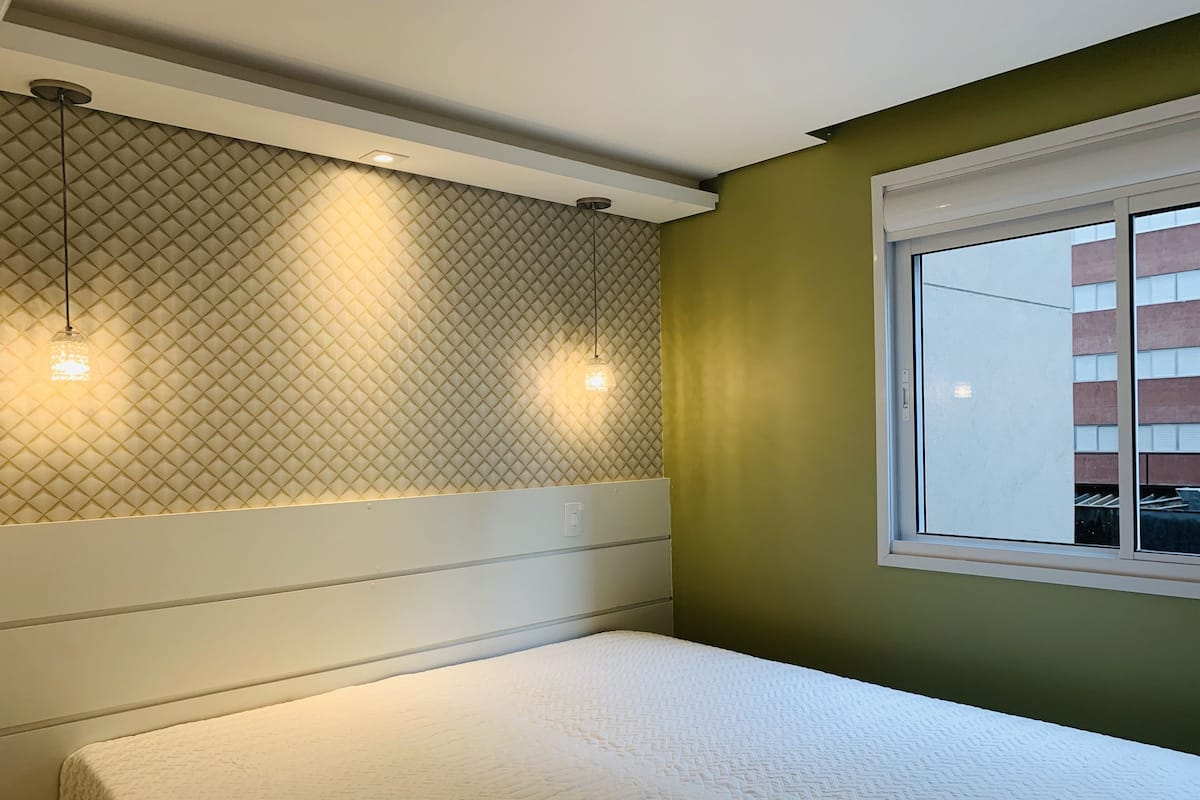 A room with a bed, a window, and a wall with a geometric pattern.