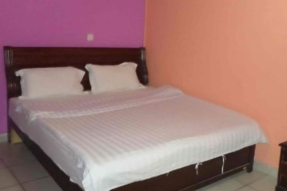 Quarto com cama de madeira, duas almofadas e um cobreleiro branco.