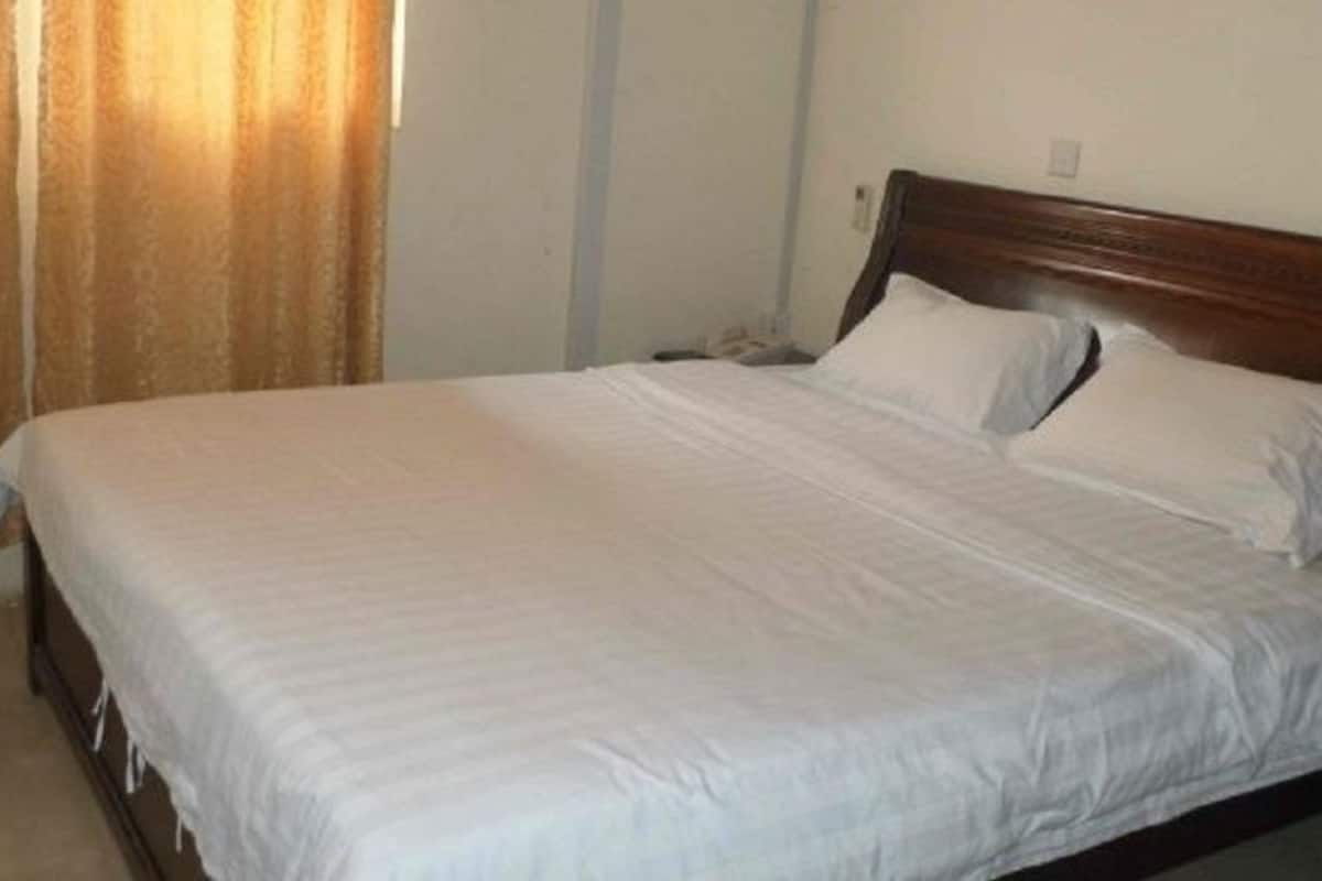 Quarto de hotel padrão com uma cama de solteiro, cabeceira de madeira e cortina na janela.