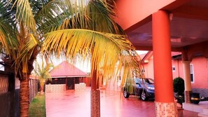 Un espacio al aire libre cubierto con palmeras, un coche y un edificio de techo rojo.