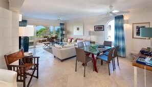 A spacious living area with a glass dining table, comfortable seating, and a view of the outdoors.