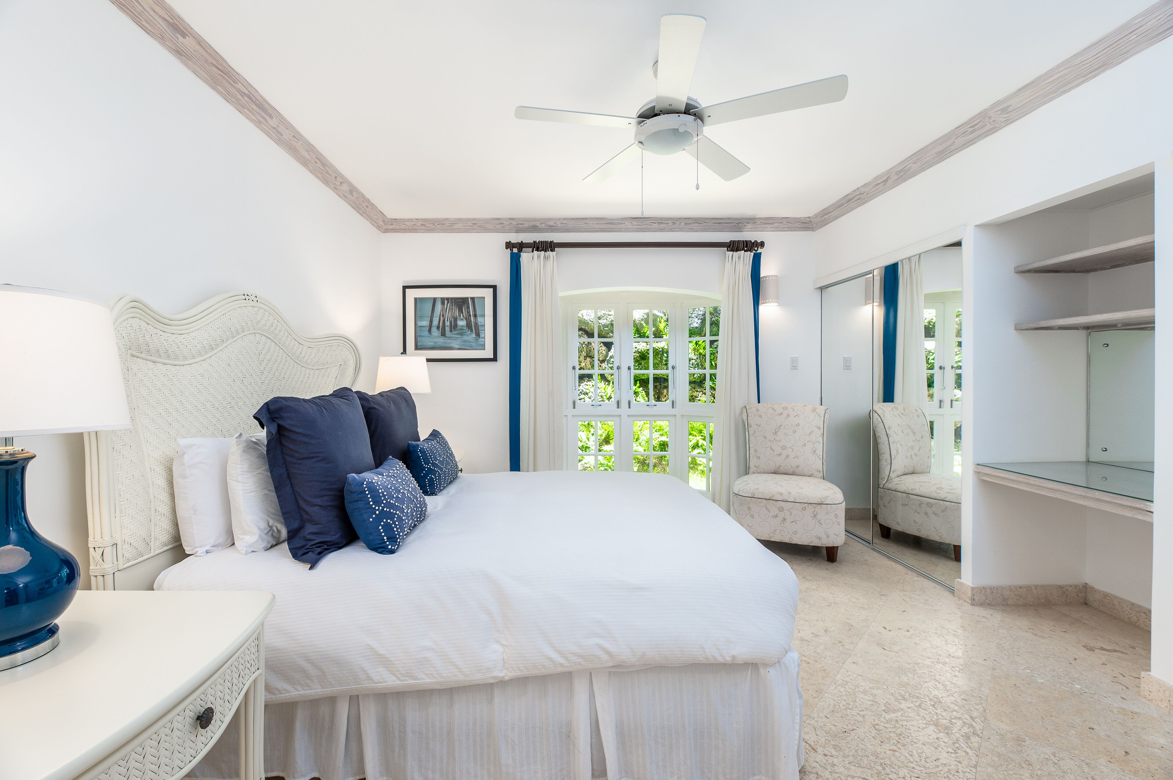 A bedroom with a bed, a ceiling fan, a chair, a nightstand, and a window with curtains.