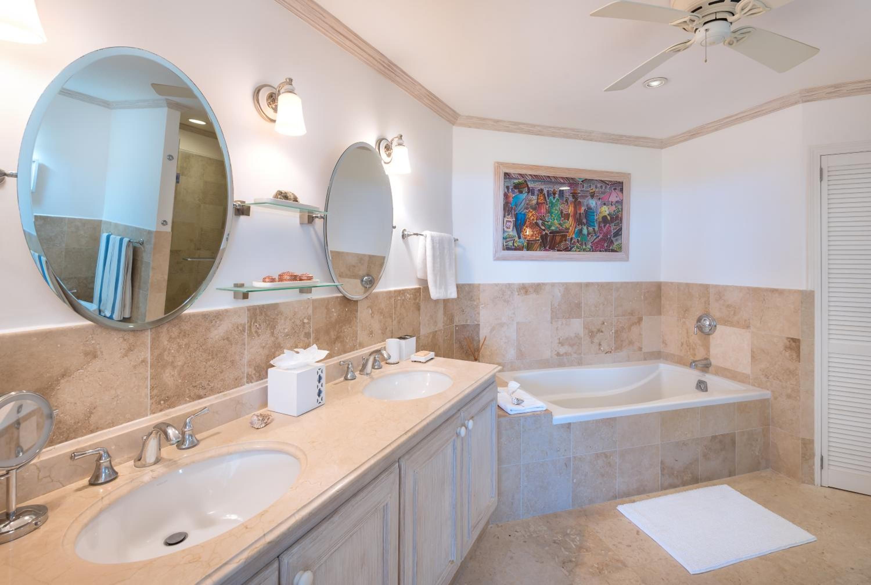 A bathroom with two sinks, a large mirror, a ceiling fan, and a colorful artwork on the wall.