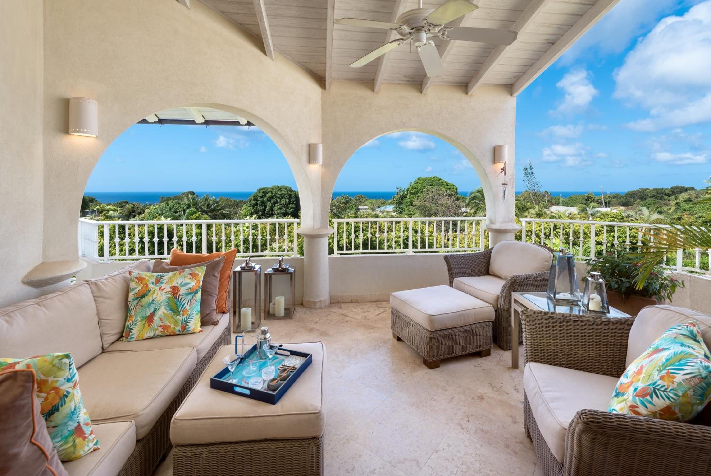 A covered outdoor seating area with wicker furniture, a ceiling fan, and a view of the ocean.