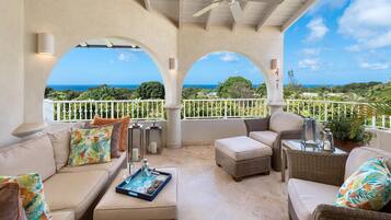 A covered outdoor seating area with wicker furniture, a ceiling fan, and a view of the ocean.