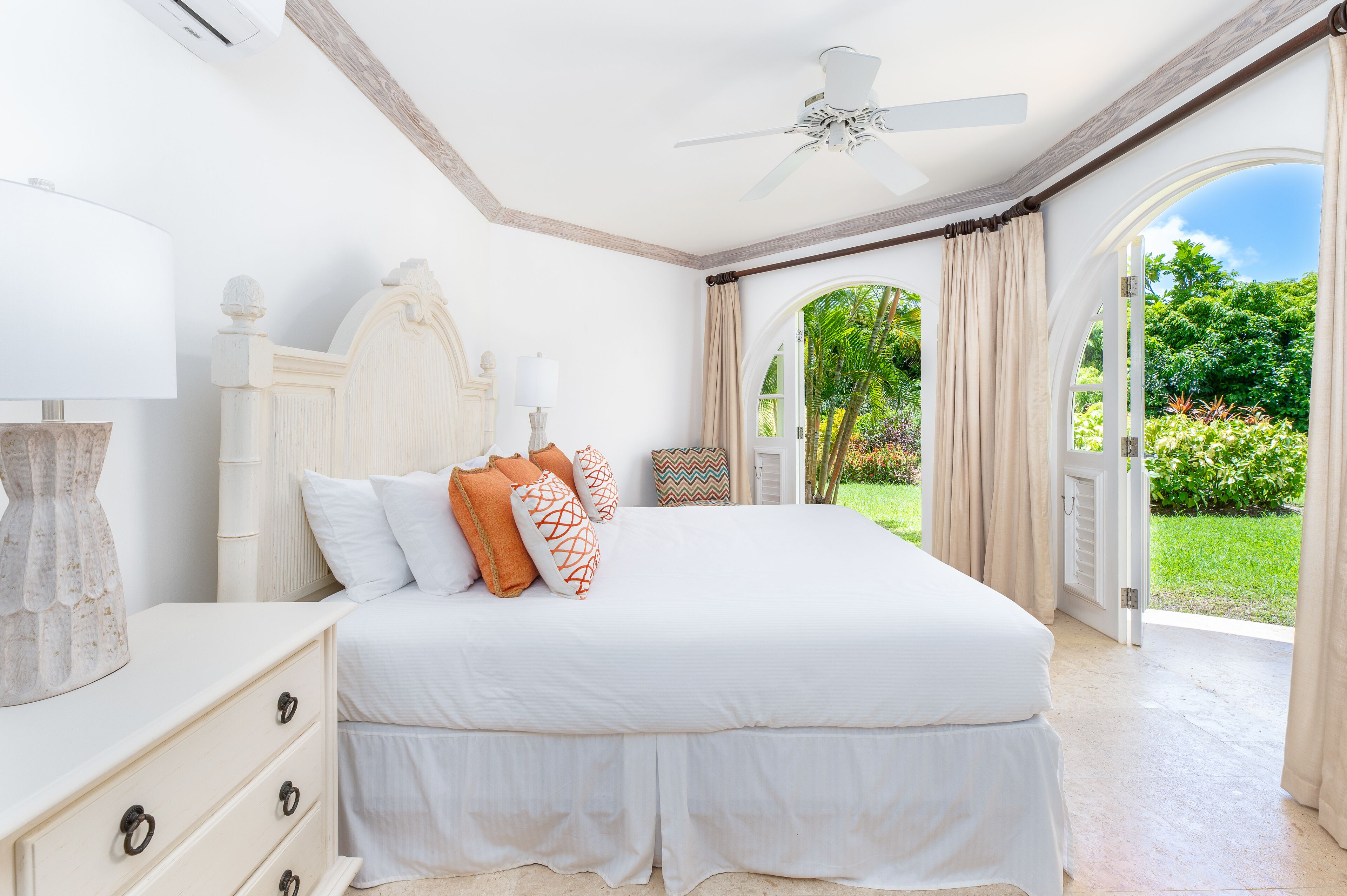Un dormitorio con una cama grande, un ventilador de techo y vistas a un jardín a través de una puerta abierta.