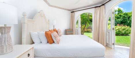 Un dormitorio con una cama grande, un ventilador de techo y vistas a un jardín a través de una puerta abierta.
