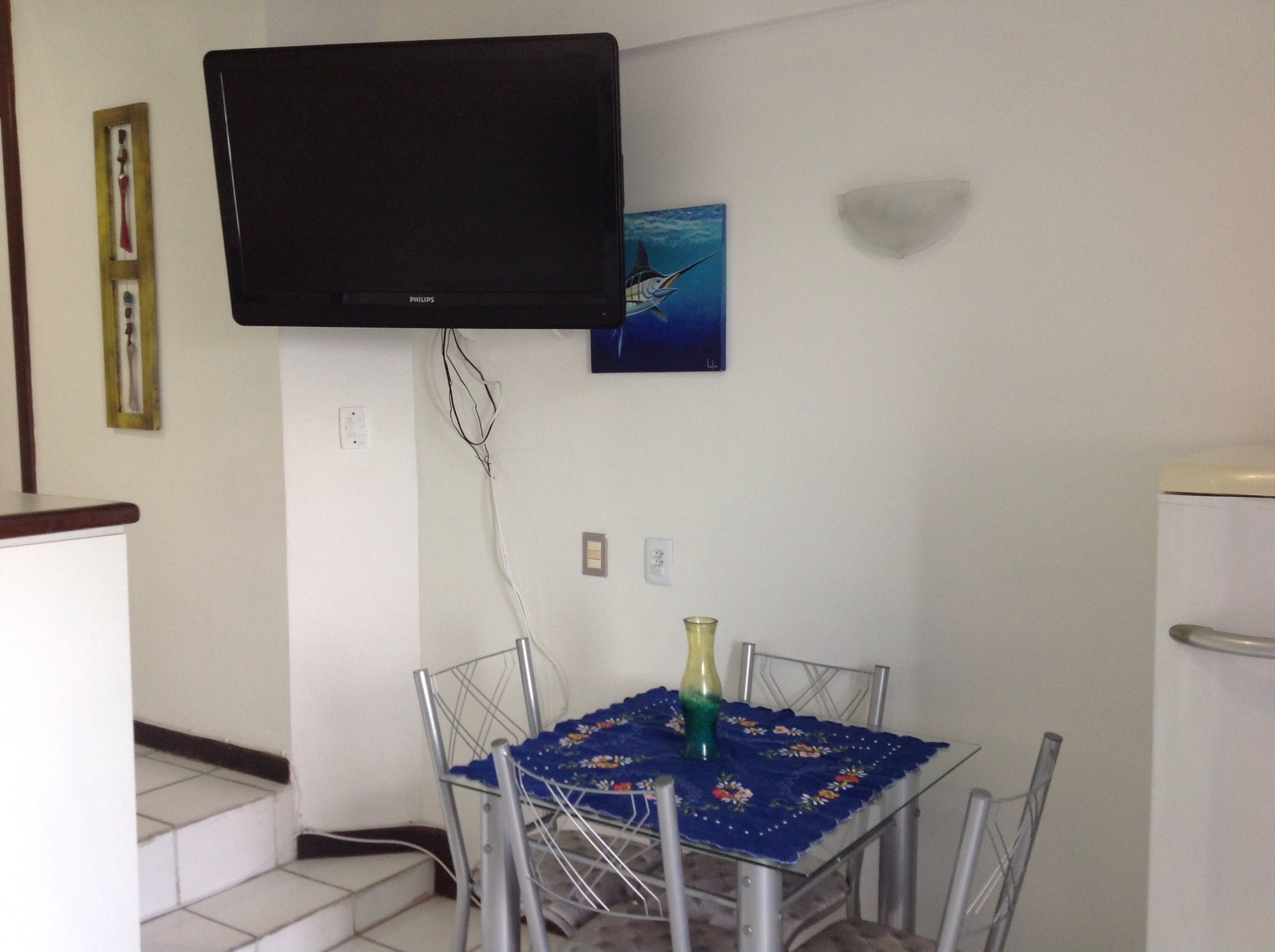 A small dining area with a table, chairs, a television mounted on the wall, and a painting.