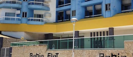 Un edificio moderno con fachada plana, varios balcones y una pared texturizada con el nombre "Bahia Flat".