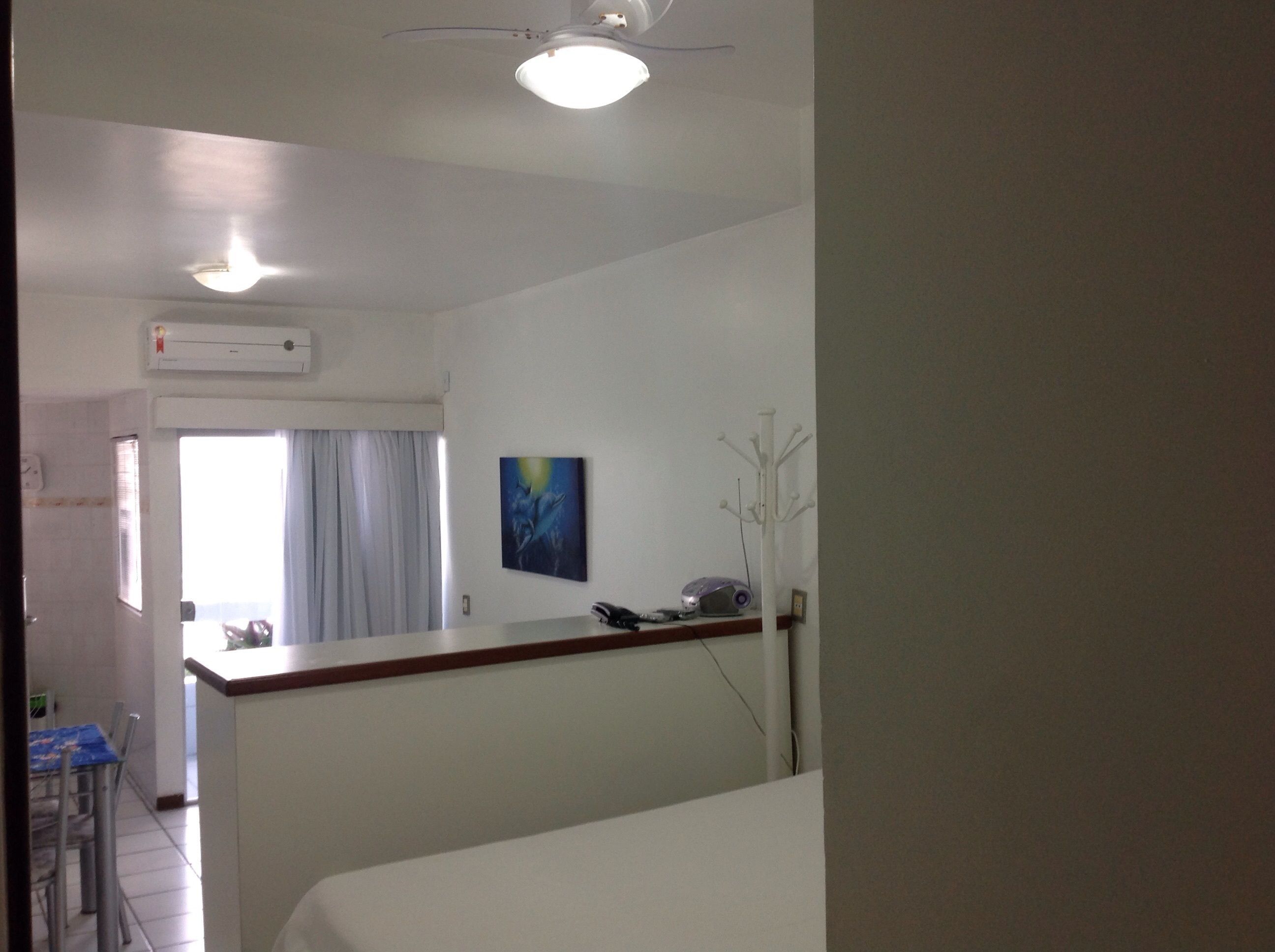 A hotel room with a bed, a desk, a chair, a coat rack, and a painting on the wall.
