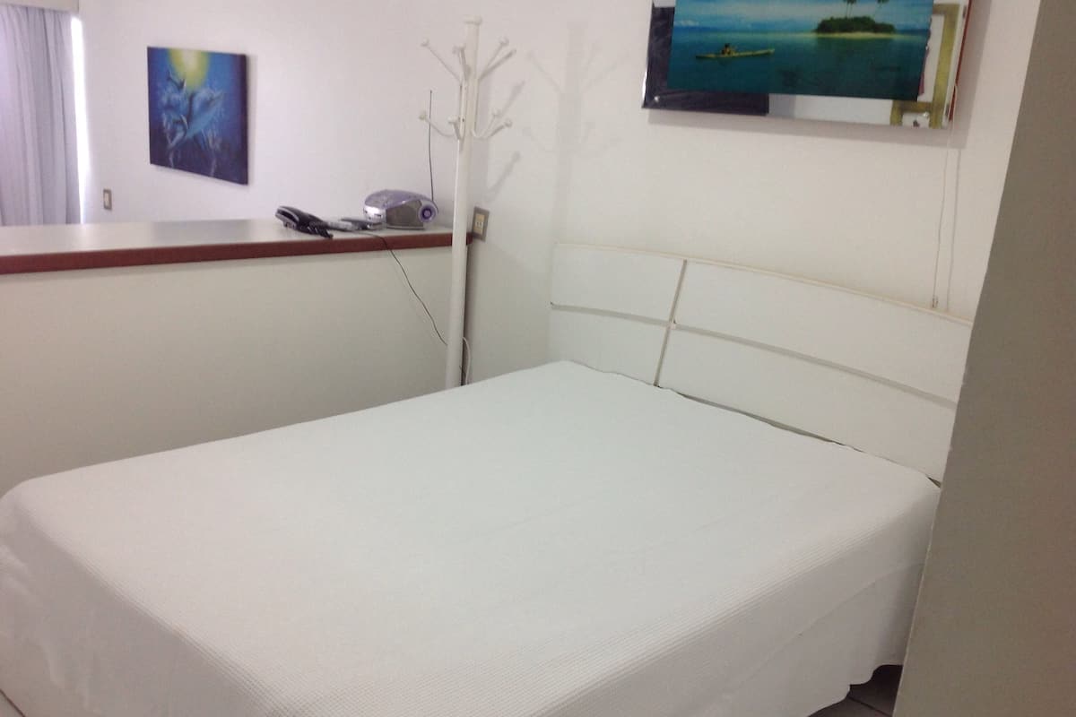 A single bed in a room with a white headboard, a painting on the wall, and a coat rack.
