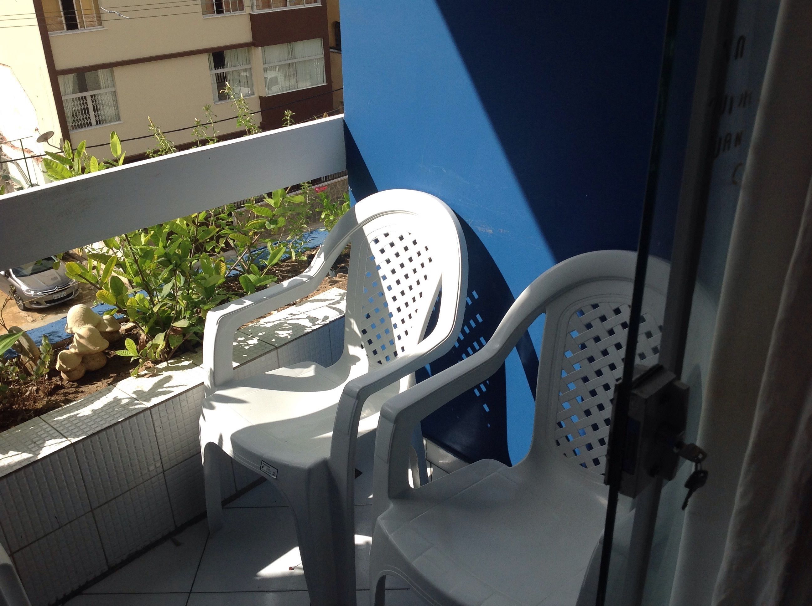 A balcony with two white plastic chairs, a tiled floor, and a view of a building in the background.
