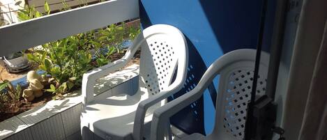 A balcony with two white plastic chairs, a tiled floor, and a view of a building in the background.