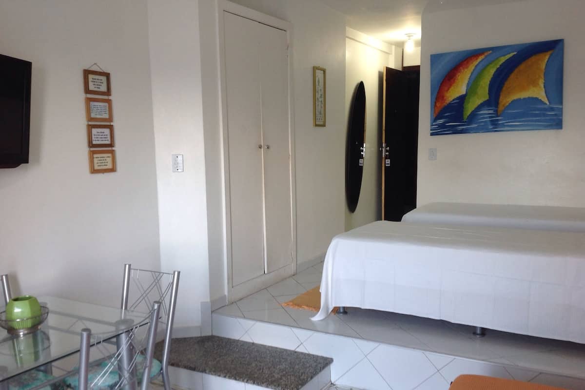 A hotel room with a bed, a chair, a table with a bowl, and a painting on the wall.