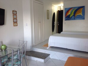 A hotel room with a bed, a chair, a table with a bowl, and a painting on the wall. - Bahia Flat Studio (Salvador)