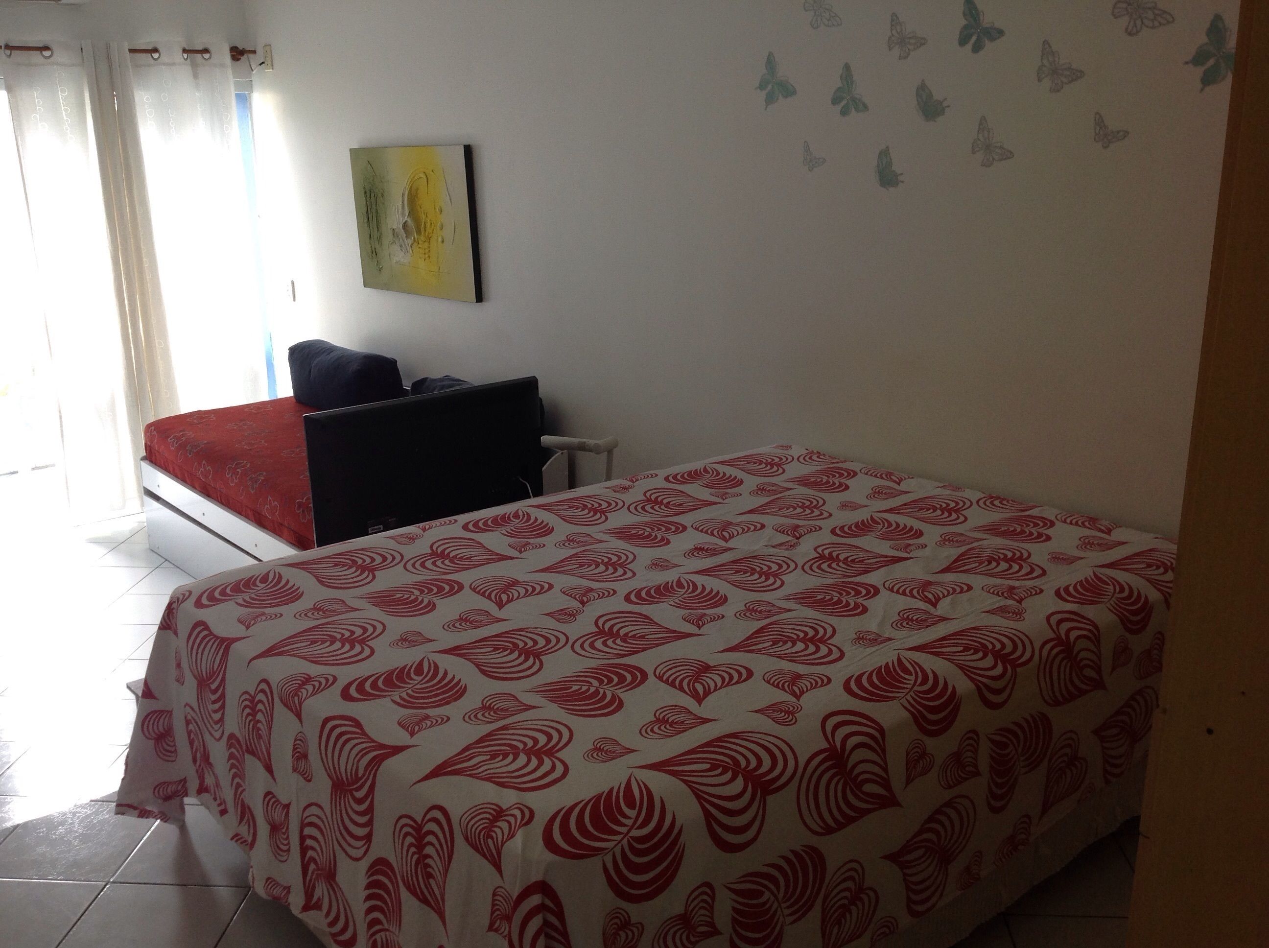 Een slaapkamer met een bed, een bureau, een stoel, een televisie en een muur met vlinderstickers.
