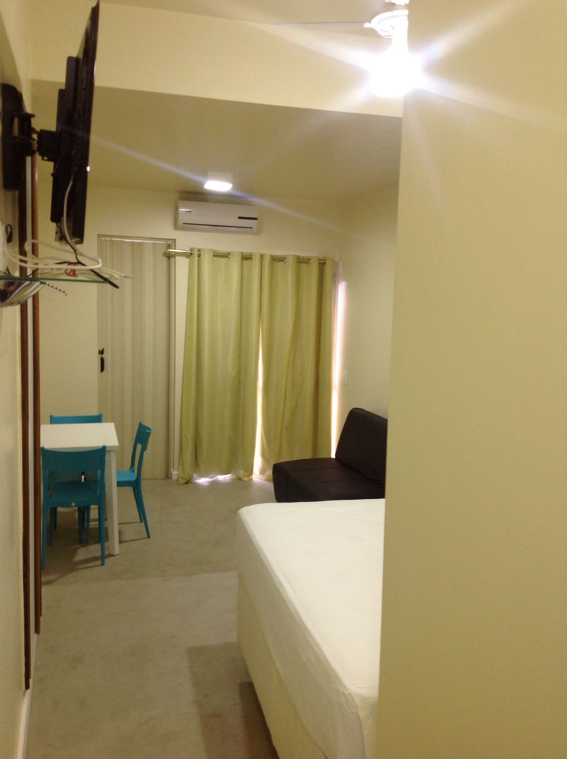 A hotel room with a bed, a desk with a chair, a TV, and a window with curtains.