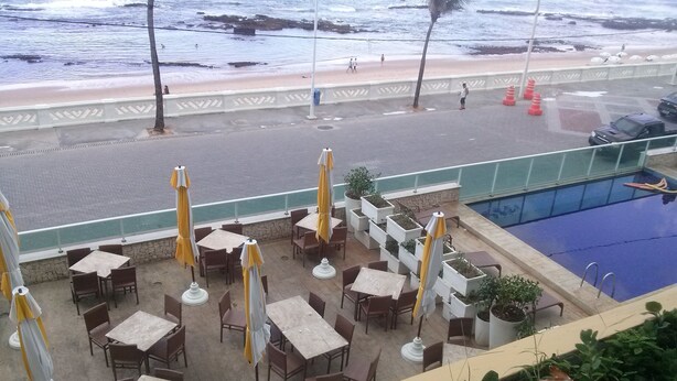 An outdoor seating area with tables and chairs, a pool, and a view of the beach. - Bahia Flat Studio (Salvador)