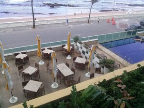 An outdoor seating area with tables and chairs, a pool, and a view of the beach. - Bahia Flat Studio (Salvador)