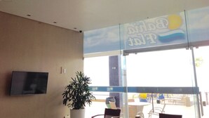 A hotel lobby with a large window, a potted plant, and a flat-screen TV mounted on the wall. - Bahia Flat Studio (Salvador)