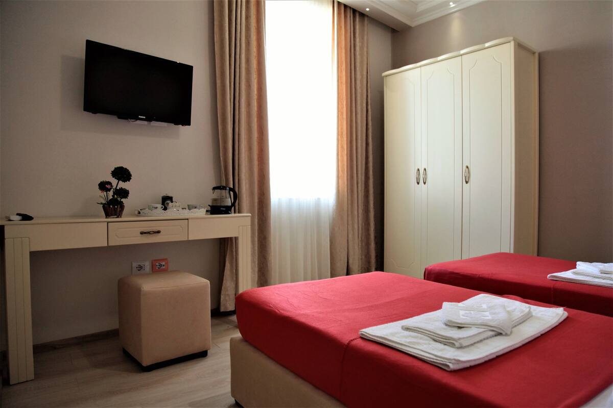 A hotel room with a TV, a desk, a wardrobe, two beds, and a window with curtains.
