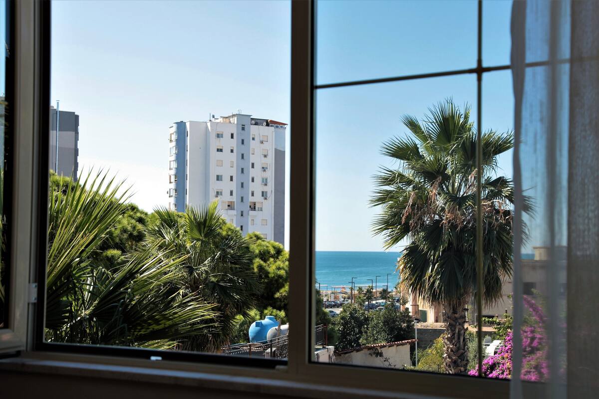 A view through a window of a tall building with a clear blue sky and a body of water in the background.