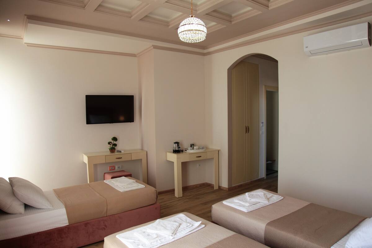 A hotel room with two beds, a desk, a TV, and an air conditioning unit.