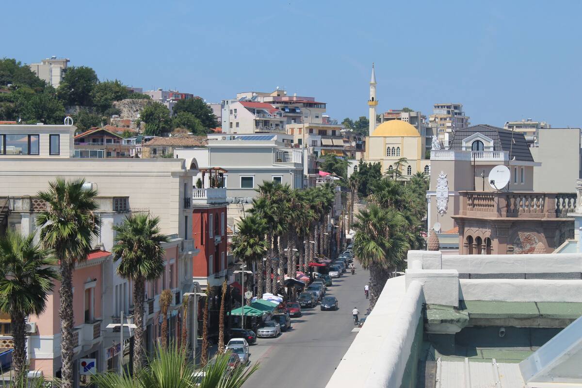 A street lined with palm trees and buildings, including a mosque with a minaret.