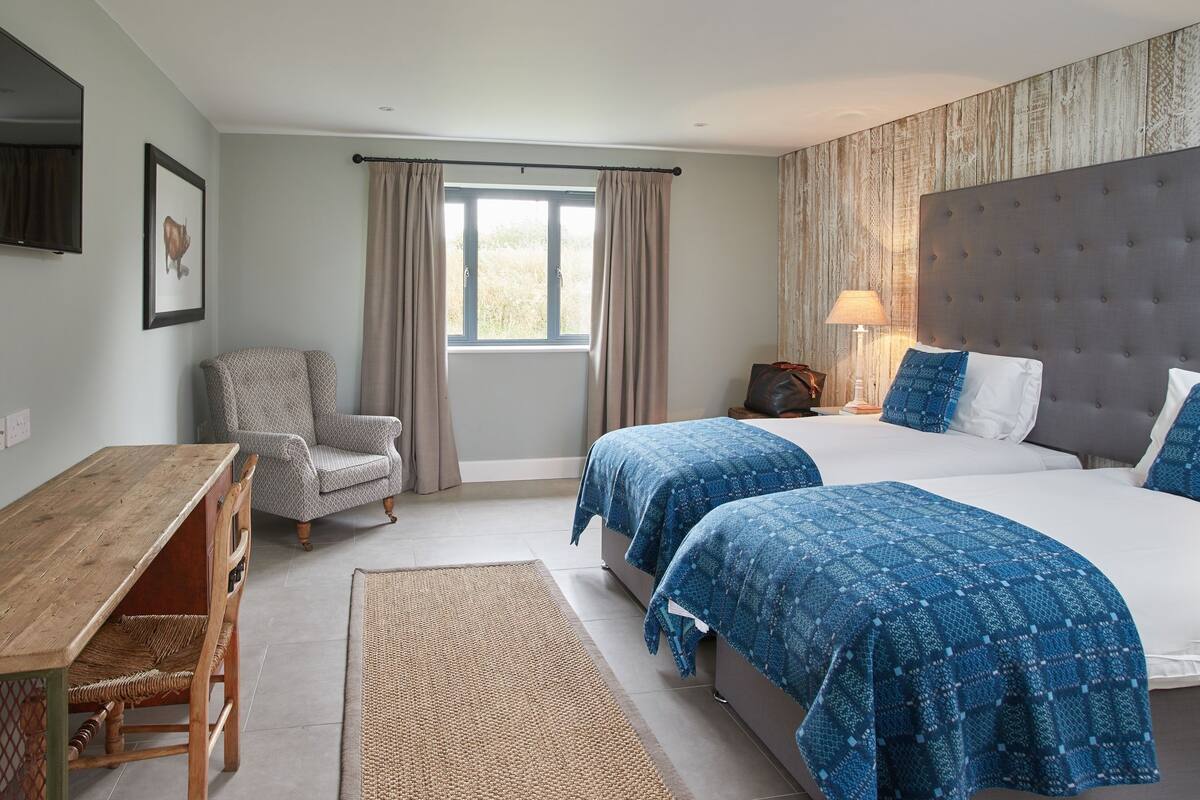 A hotel room with two beds, a desk, a chair, a window with curtains, and a mounted television.