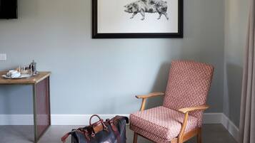 A room with a framed animal print on the wall, a wooden chair, a desk with a tray of cups, and a bag on the floor.