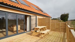 A wooden deck with a picnic table, sliding glass doors, and a tiled roof. - The Pig Shed Motel (King's Lynn)