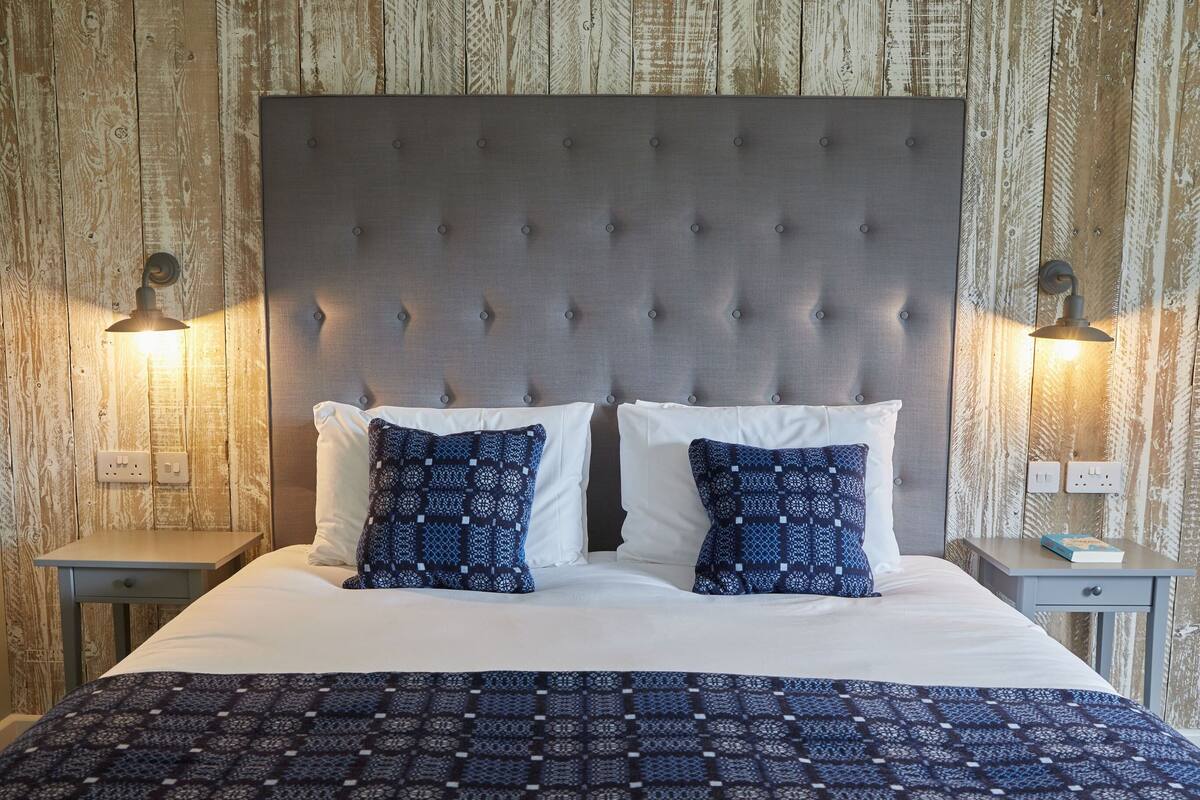 A neatly made bed with a patterned bedspread, two pillows, and a tufted headboard. There are two bedside tables with lamps and a book on one.