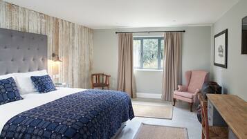 A bedroom with a large bed, a wooden headboard, a chair, a desk, and a window with curtains.