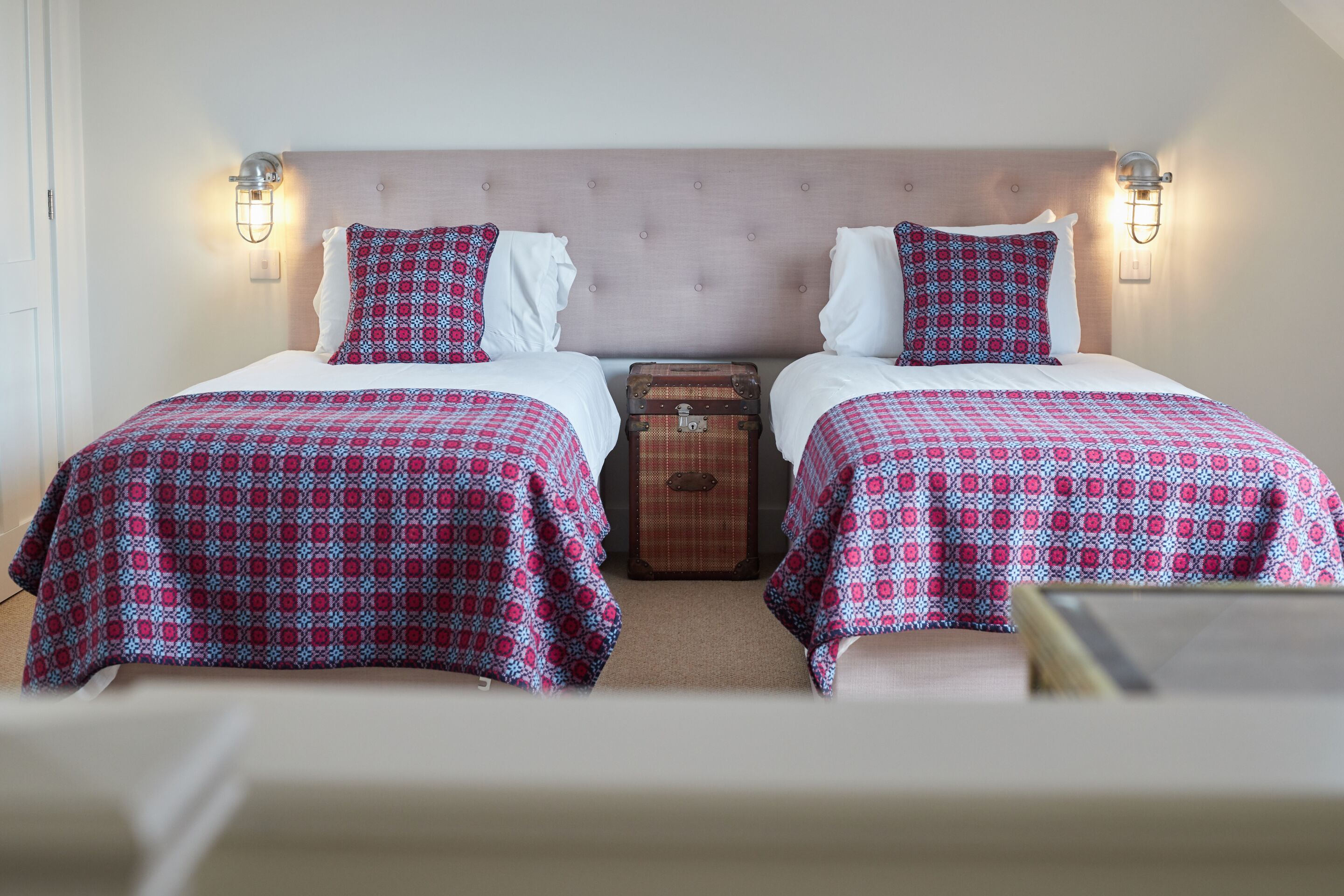 A double room with two beds, each with a patterned bedspread and matching pillows, a wooden chest of drawers, and wall-mounted light fixtures.