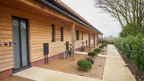 A row of wooden cabins with a covered walkway, bicycles, and a well-maintained garden. - The Pig Shed Motel (King's Lynn)