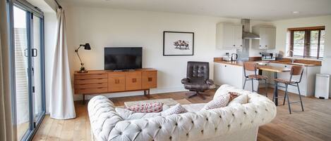 A living room with a sofa, a TV, a wooden cabinet, and a kitchen area with a counter and chairs.