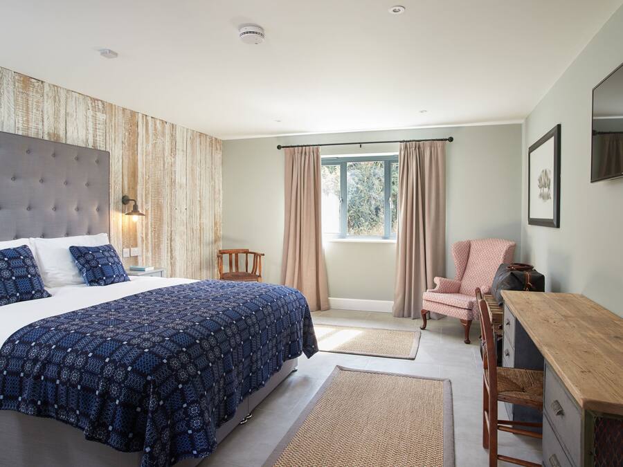 A bedroom with a large bed, a wooden nightstand, a chair, a desk, and a window with curtains.