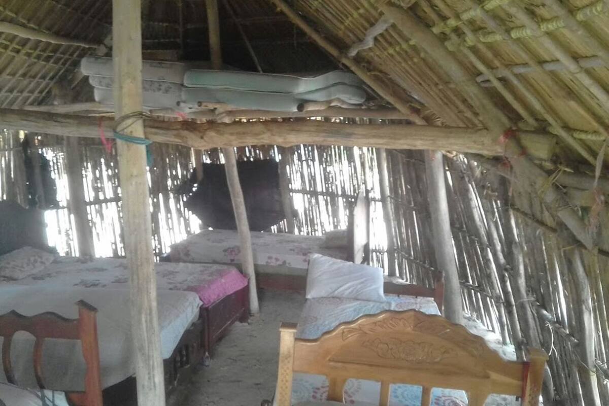A rustic room with two wooden beds, a thatched roof, and a simple wooden structure.