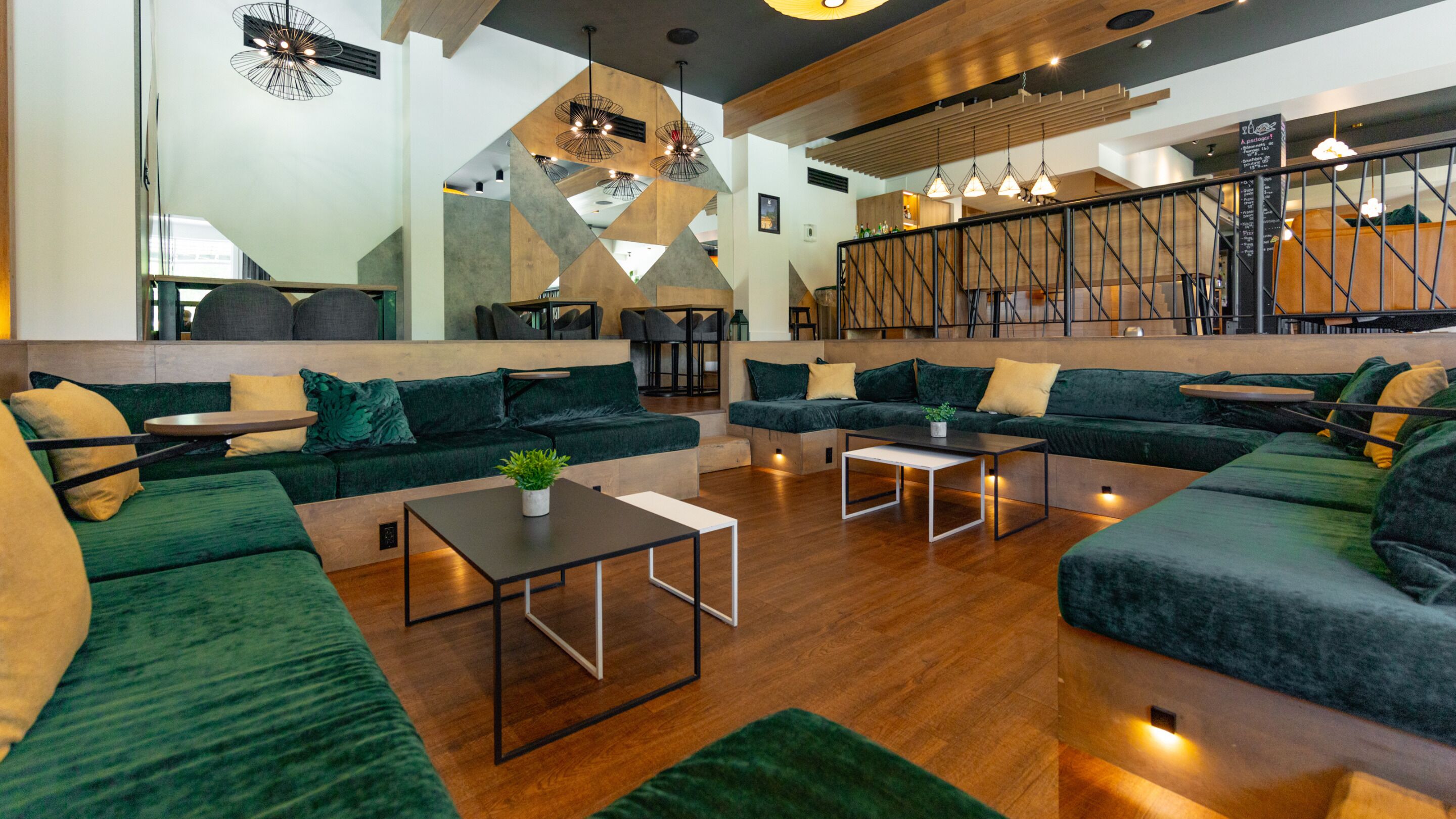 Ein stilvoller Lounge-Bereich mit grünen Sofas, Holzböden und Pendelleuchten.