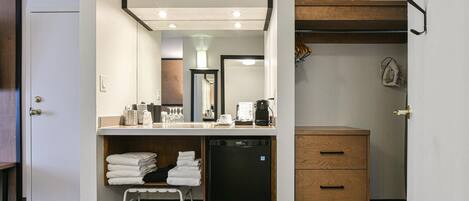Habitación de hotel con kitchenette, un refrigerador pequeño, un mueble de madera, un espejo y un lavamanos.