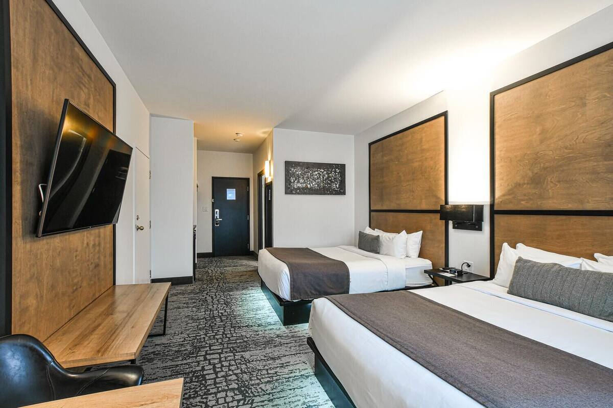 Habitación de hotel con dos camas, un escritorio, un televisor de pantalla plana y suelo alfombrado.