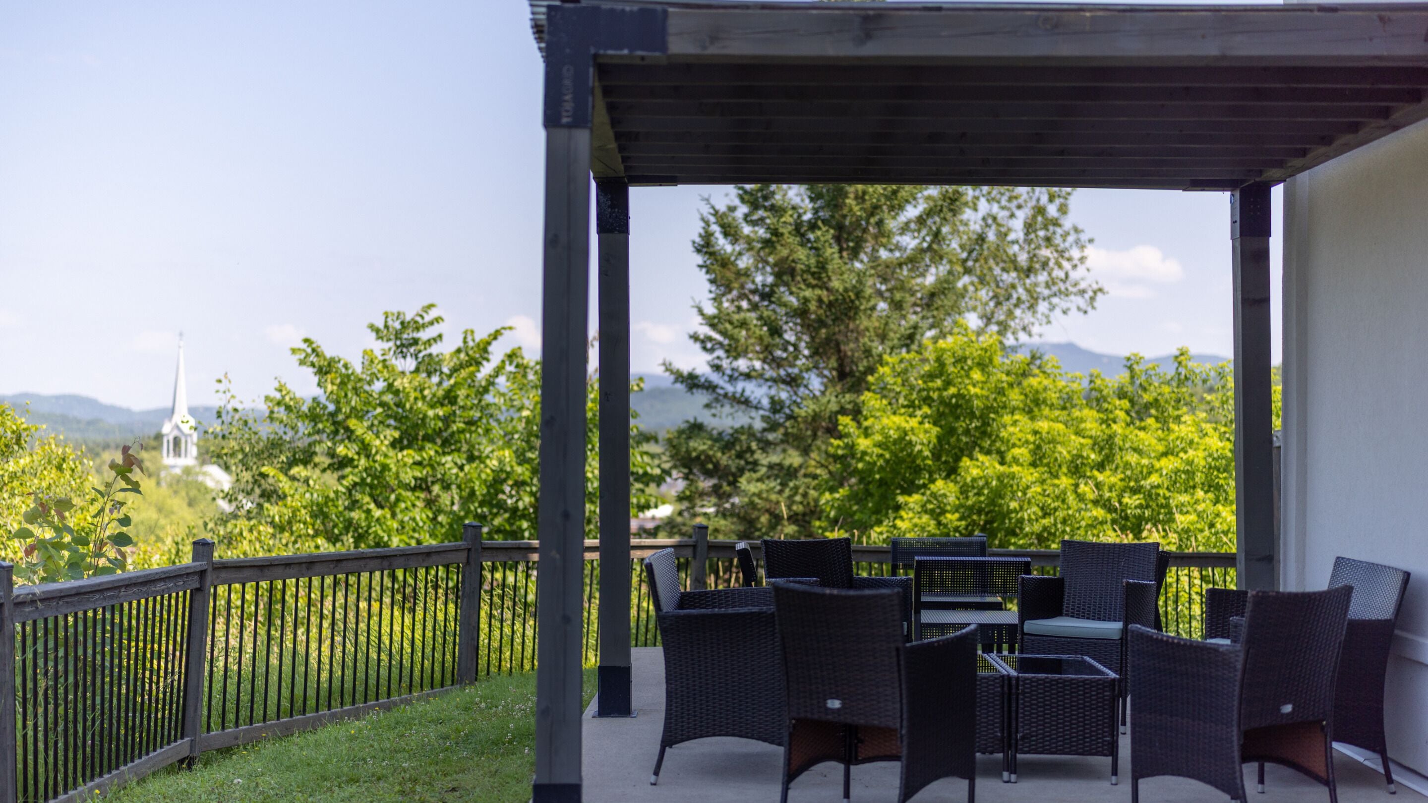 A covered outdoor seating area with wicker furniture, a view of greenery and a distant building.